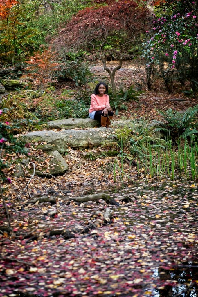 Young black girl posed on a rock near a pond with flowers and leaves