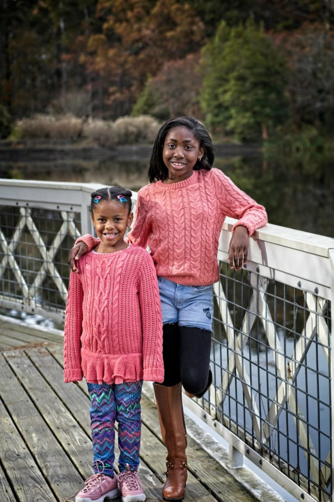 Two young black girls posed together on a deck overlooking a large pond