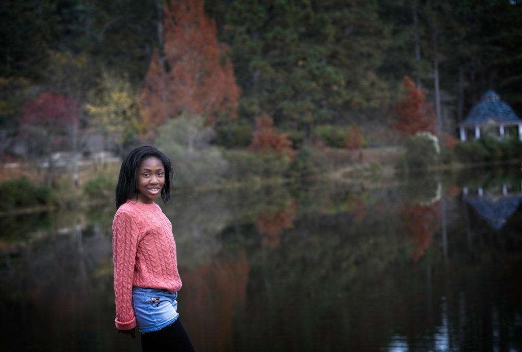 Black tween girl posing in front of pond with reflection of trees in the water