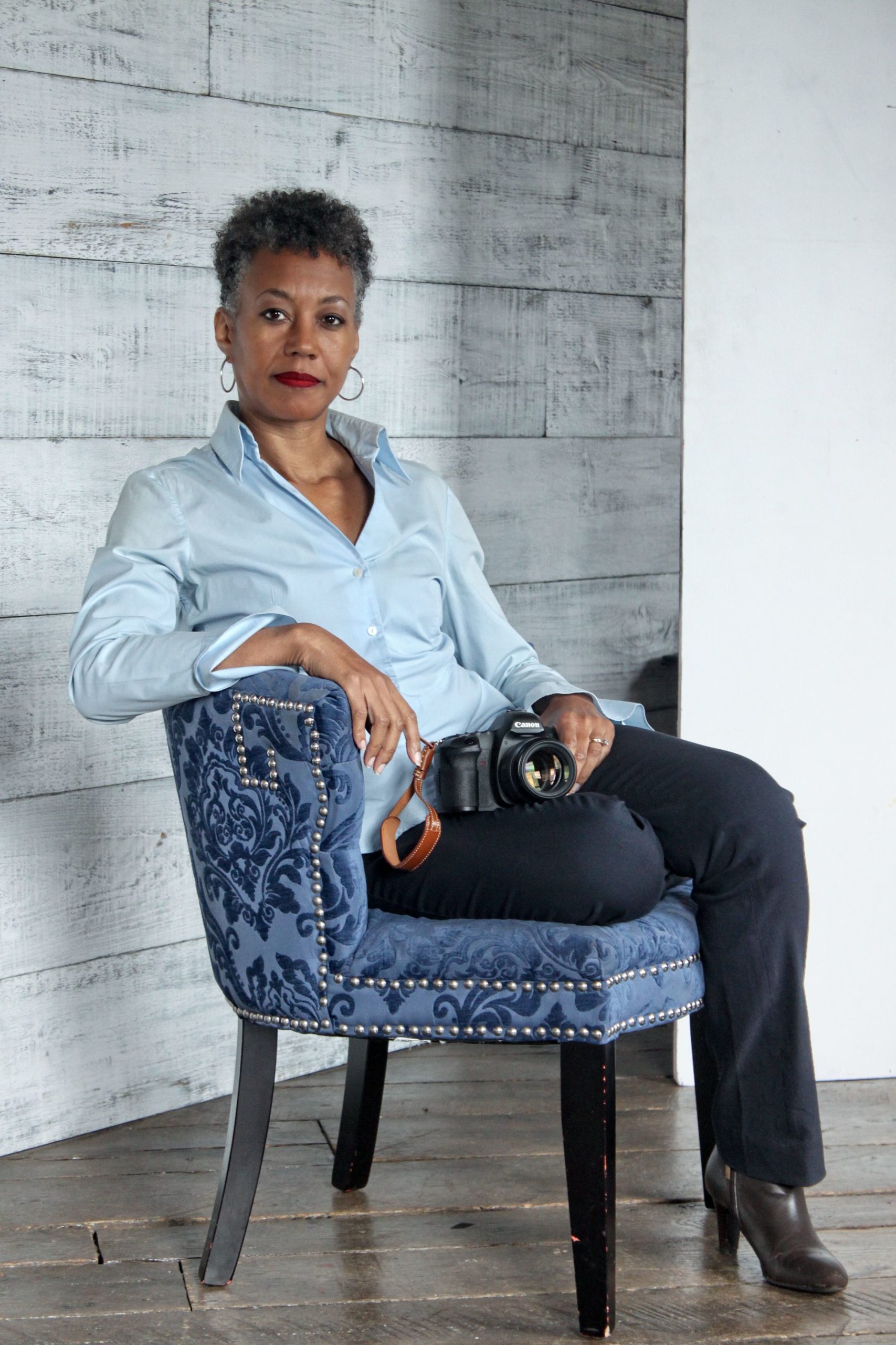 Portrait of a woman holding a camera while sitting in a chair